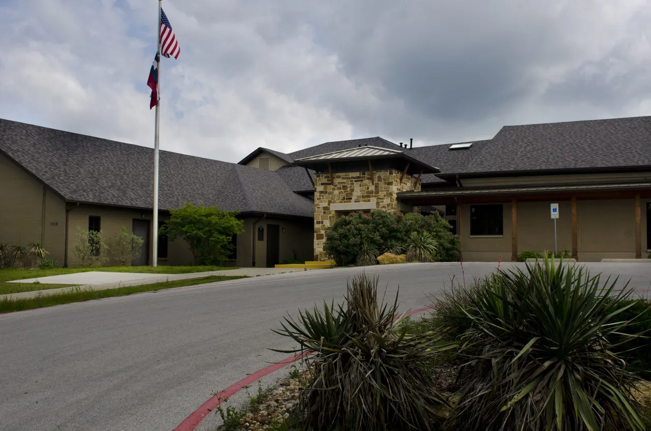 Exterior view of a single-story stone and stucco building with American and Texas flags on a flagpole.