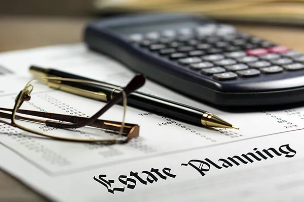 Close-up of estate planning documents with glasses, a pen, and a calculator on a desk.