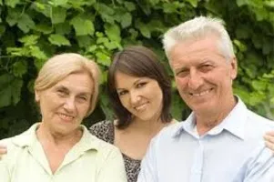 Three smiling adults, two women and one man, standing outdoors with green foliage background.
