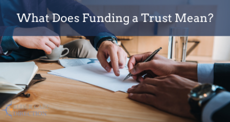 Two professionals reviewing and signing documents at a wooden table with text overlay "What Does Funding a Trust Mean?